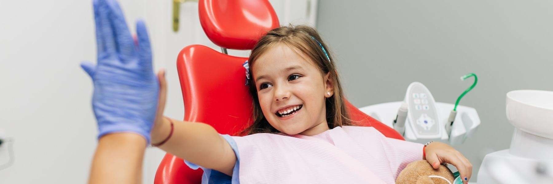 young girl giving dentist a high five in dental chair