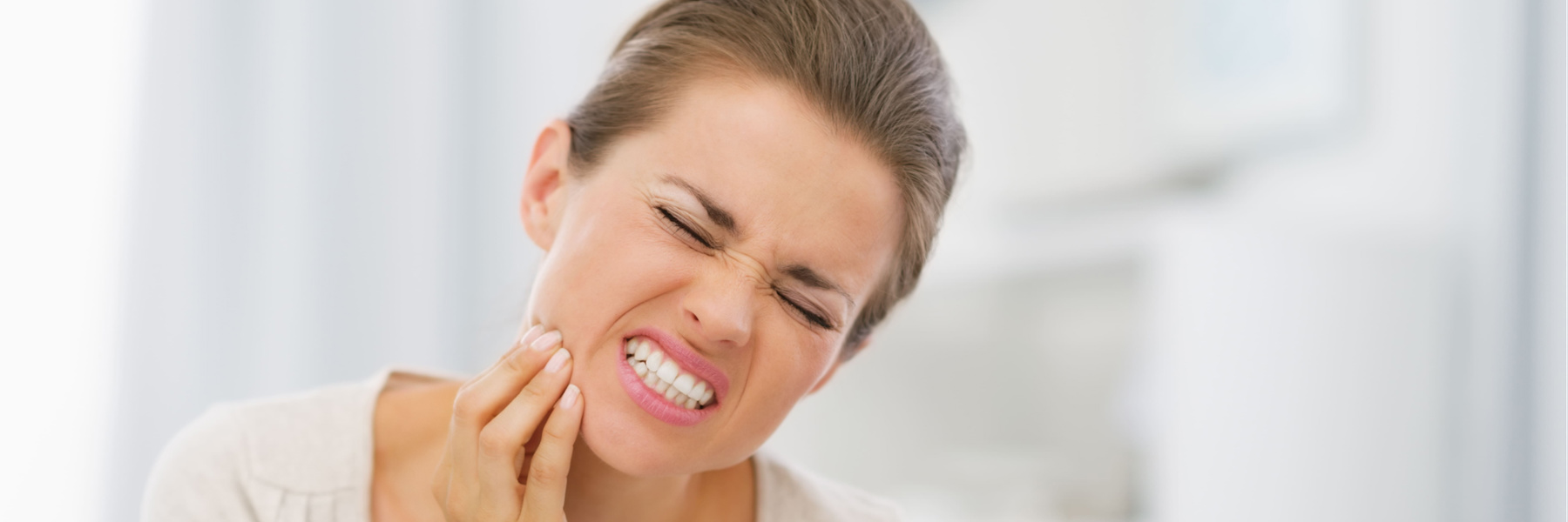 Woman grimacing in pain and holding her jaw due to a cracked tooth