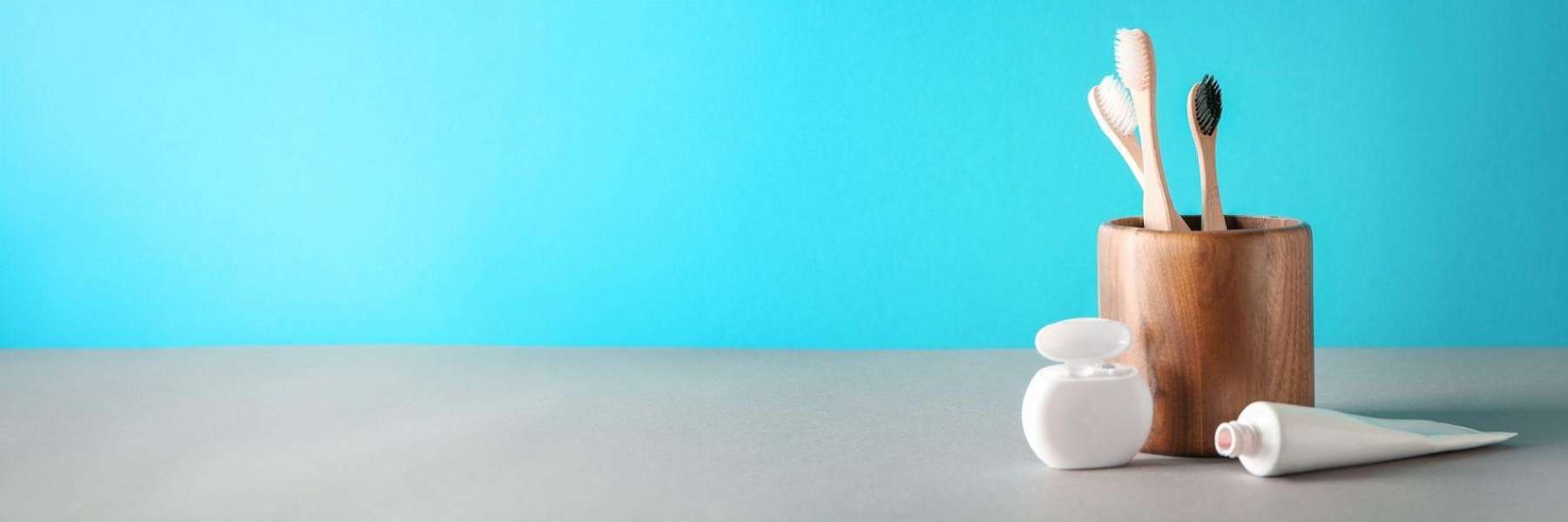 cup holding three toothbrushes with floss and toothpaste nearby