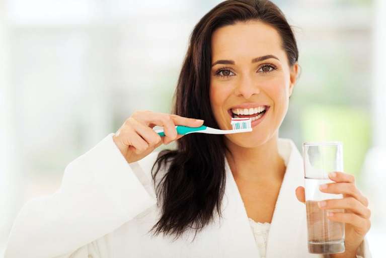 woman holding tooth brush and glass of water