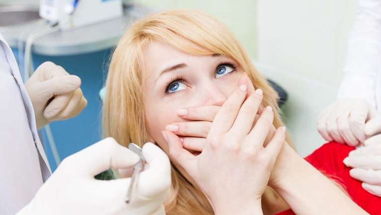 woman afraid of dentist covering her mouth while sitting in dental chair