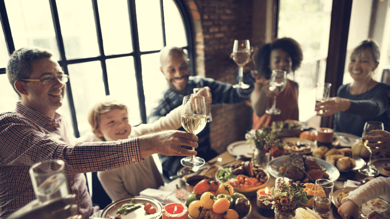 group of friends toasting with wine glasses before eating dinner