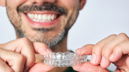 Smiling man holding a clear Invisalign aligner tray at his first consultation