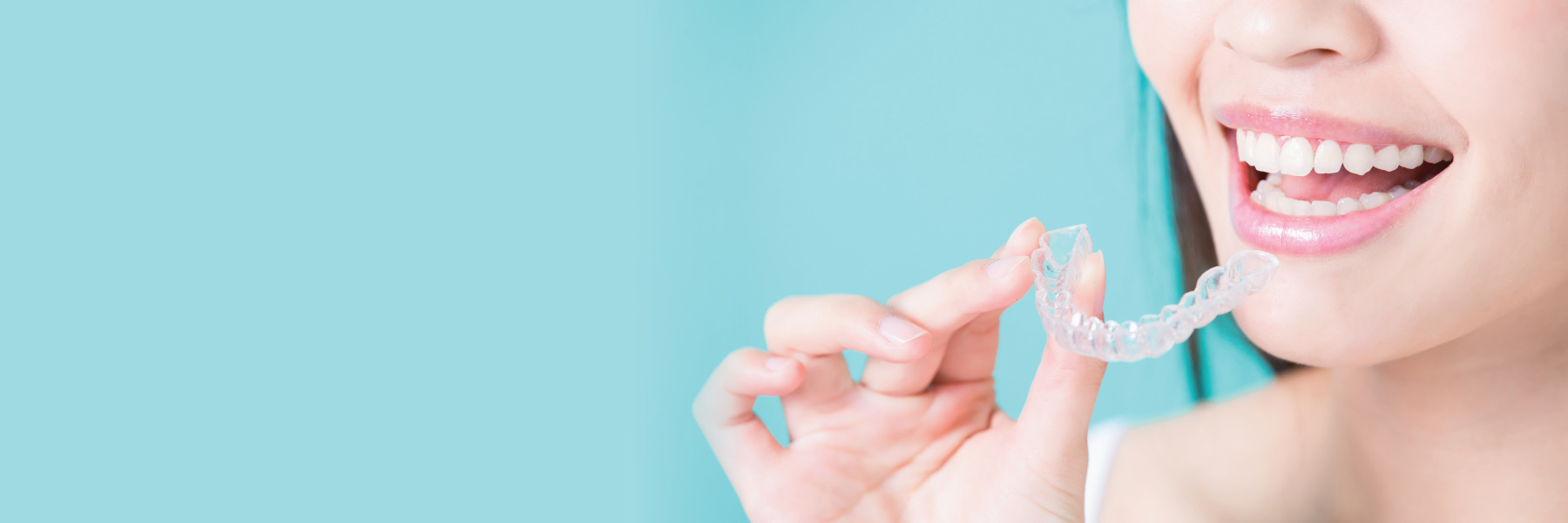 Smiling woman holding a clear Invisalign aligner tray against a teal background